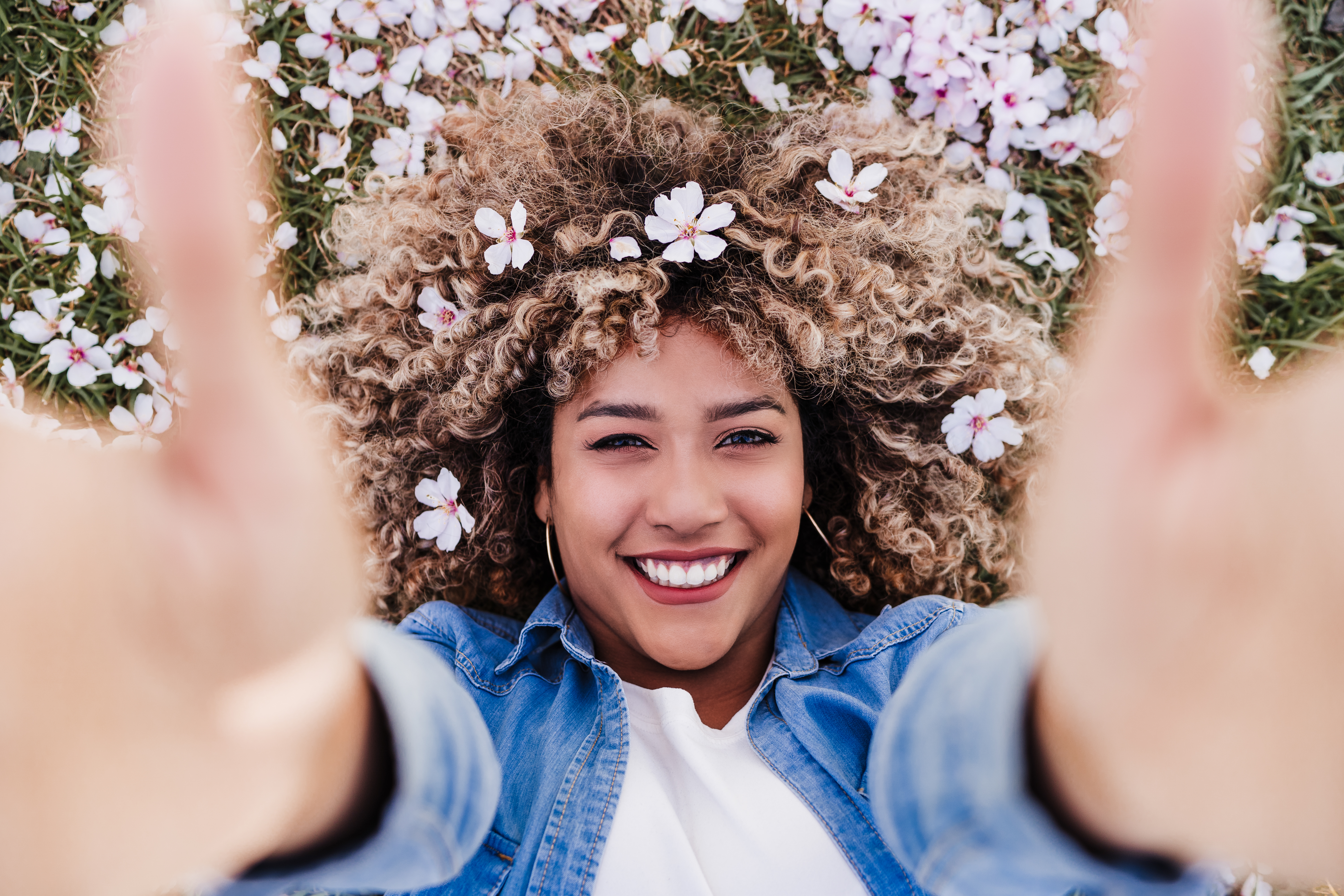 top view of happy hispanic woman with afro hair lying on grass among pink blossom flowers.Springtime